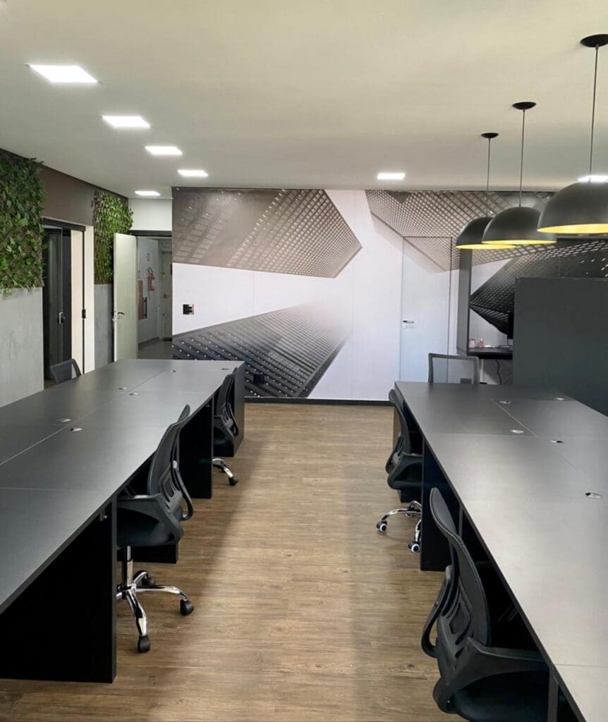Estações de trabalho do coworking na Av. Independência, com mesas pretas e mural arquitetônico